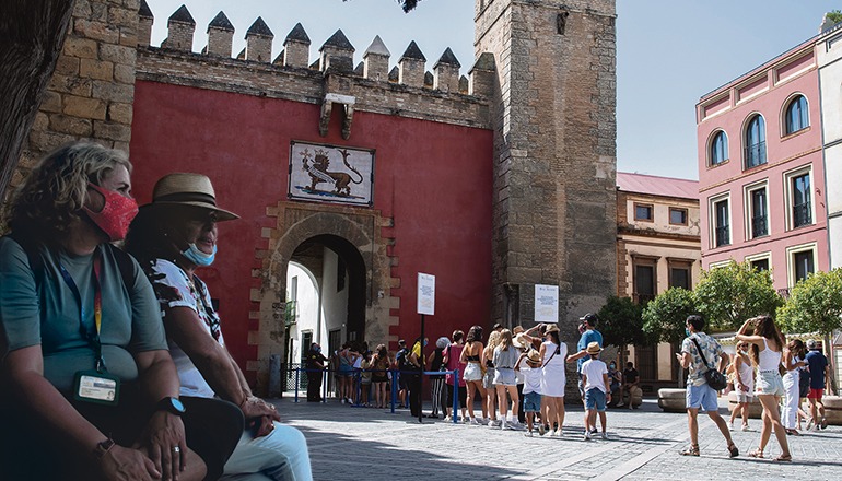 Touristen warten vor dem mittelalterliche Königspalast Alcázar von Sevilla auf Einlass. In der sommerlichen Hitze ist das Tragen von Masken besonders unangenehm, bleibt aber dennoch Pflicht. Foto: EFE